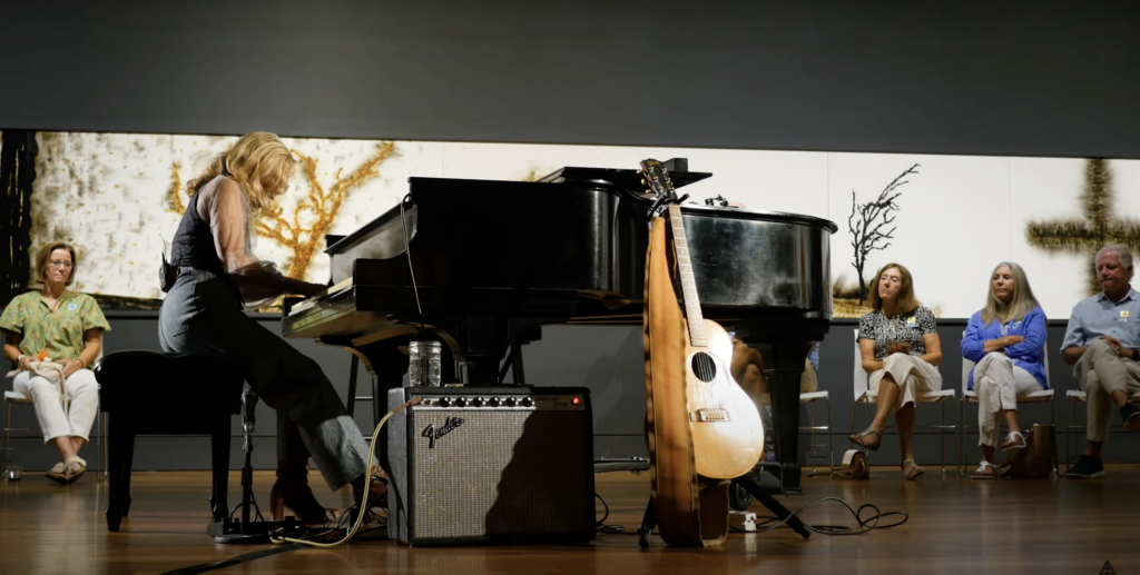 Woman playing piano and singing inside art exhibit.